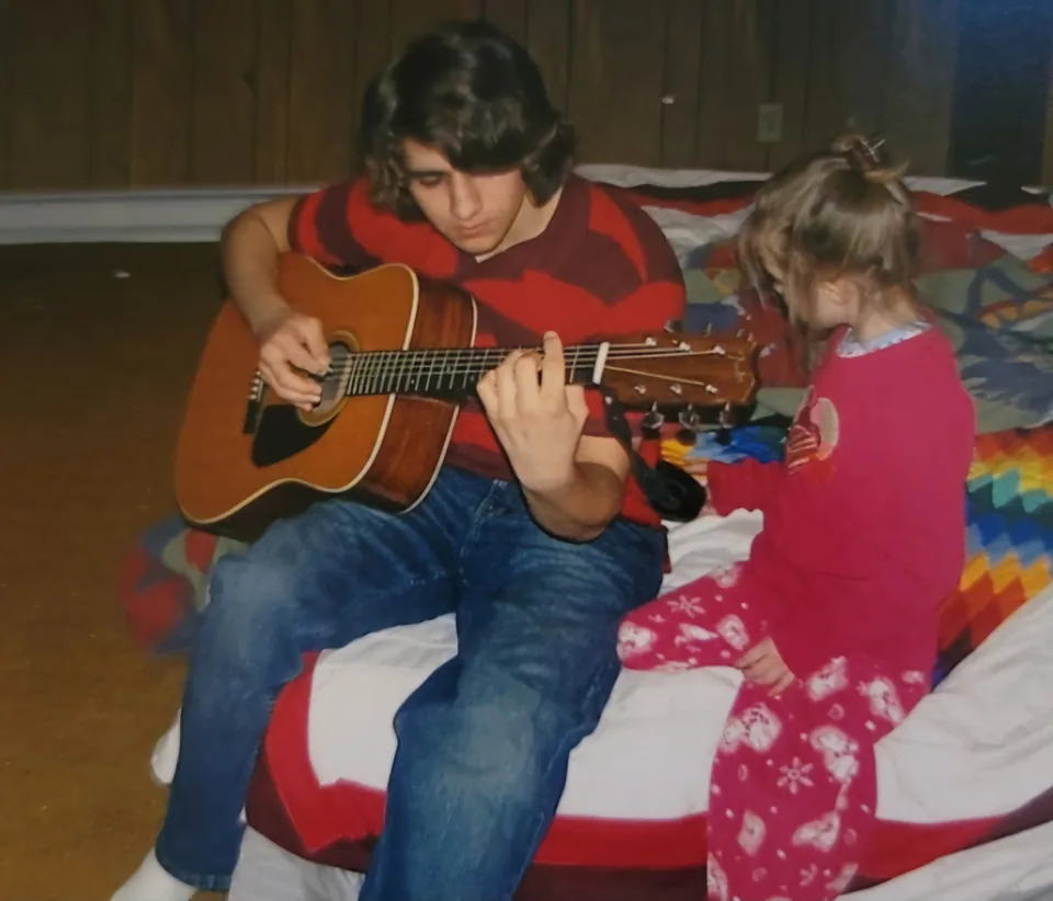 Christopher playing acoustic guitar, his younger sister seated beside him